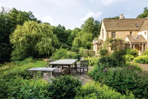 Duck Hollow - Cotswold garden designed by Rachael White House with seating area out front and green shrubs