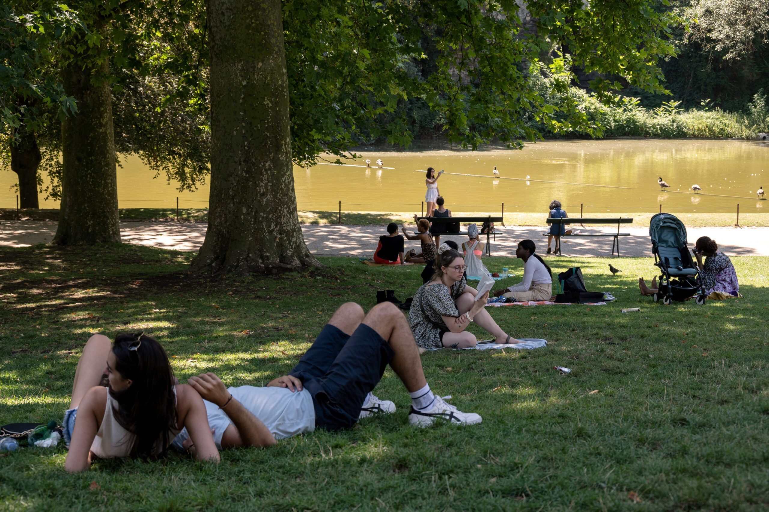 People rest in the shades of trees in Buttes Chaumont park in Paris