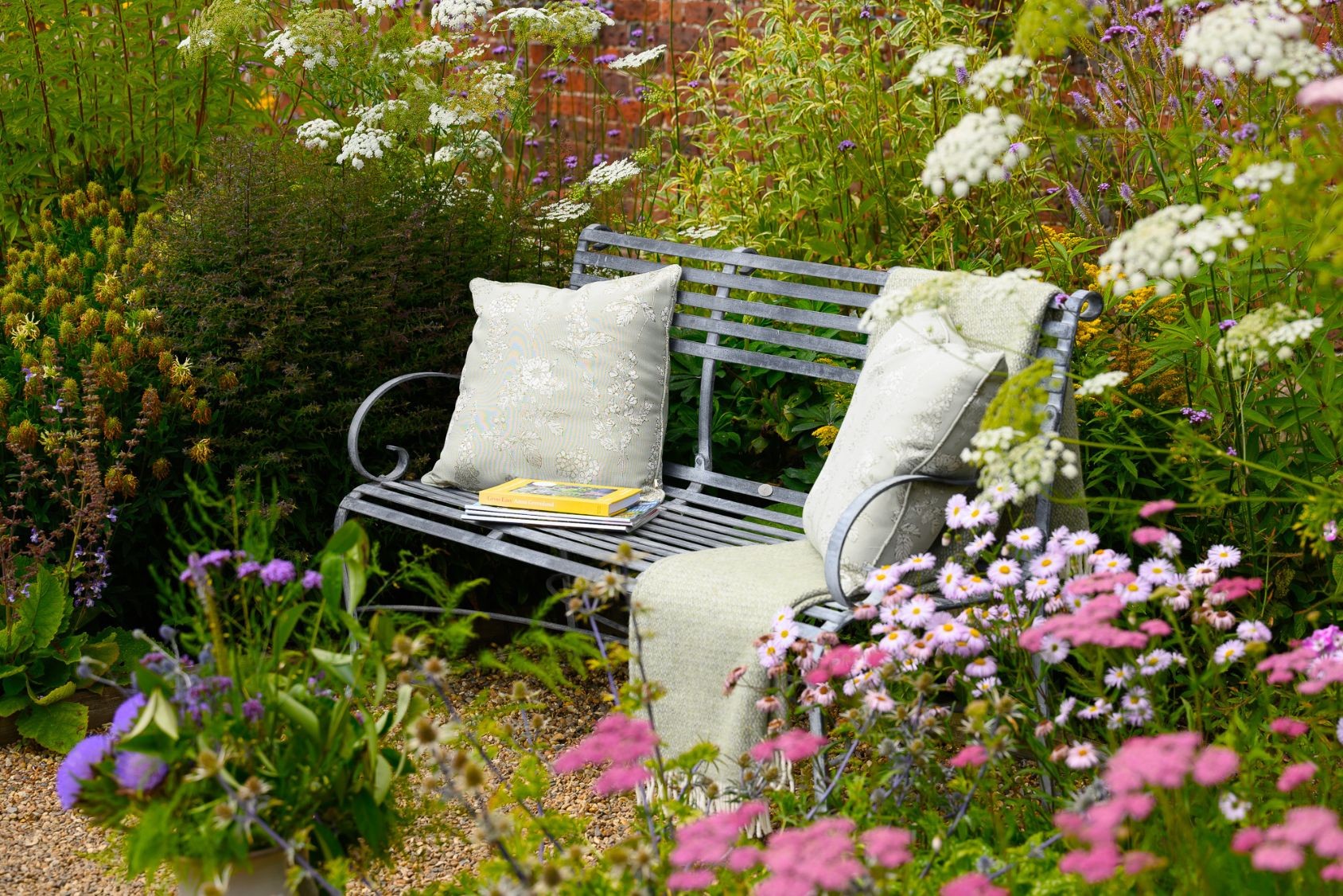 Harrod Horticultural Southwold Garden Bench with cushions and a blanket amongst foliage