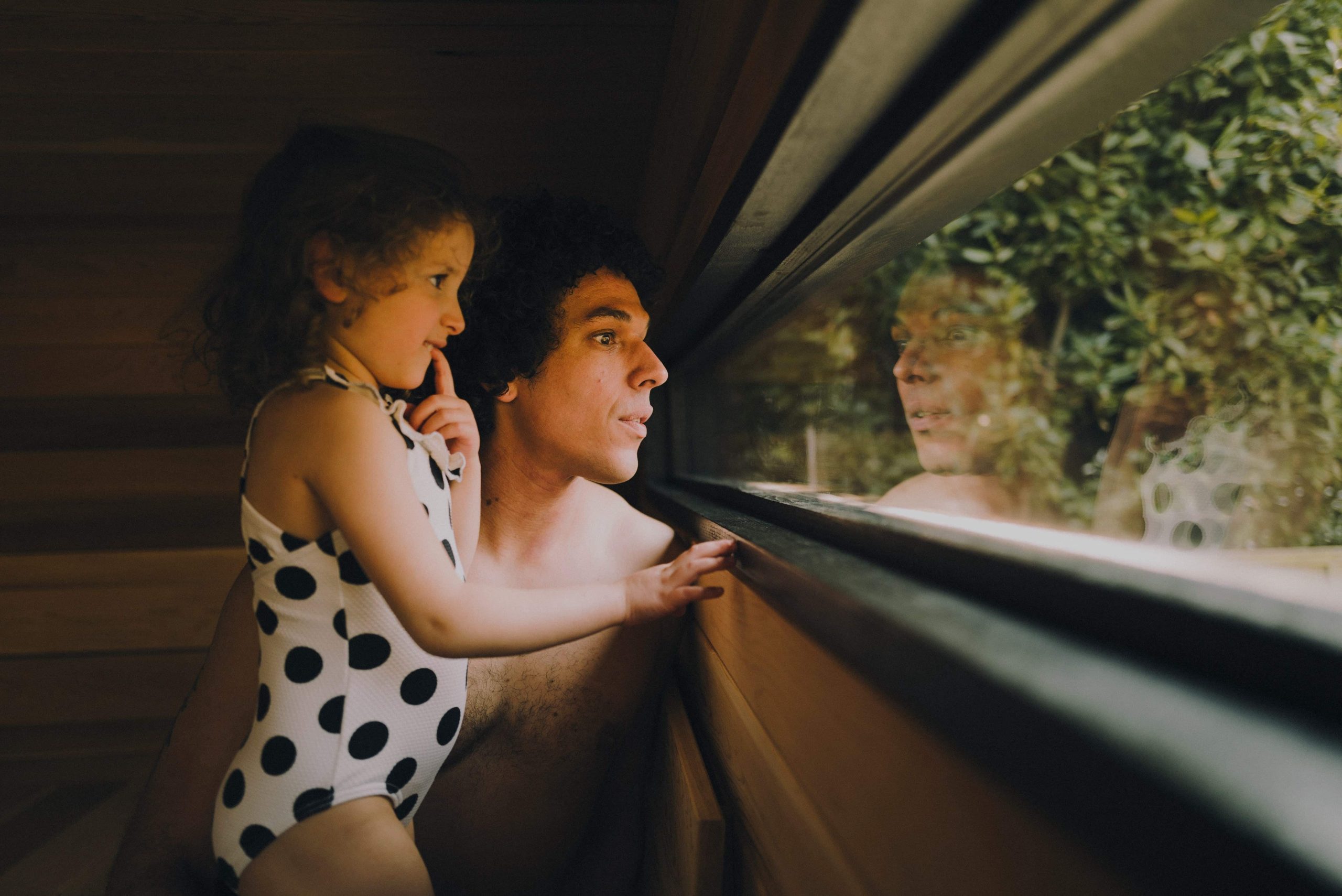 Father and daughter looking out through the window of the sauna into the garden