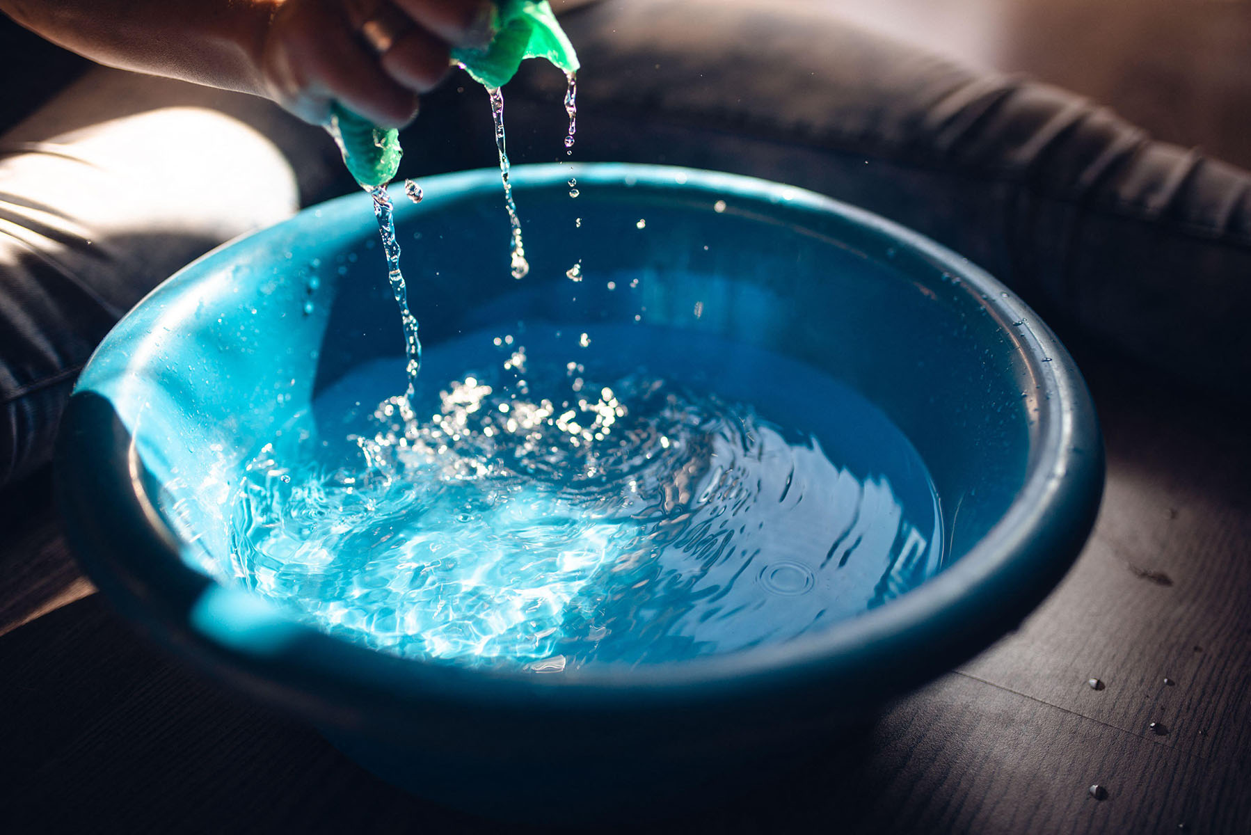 The woman squeezes a cloth over the blue bucket
