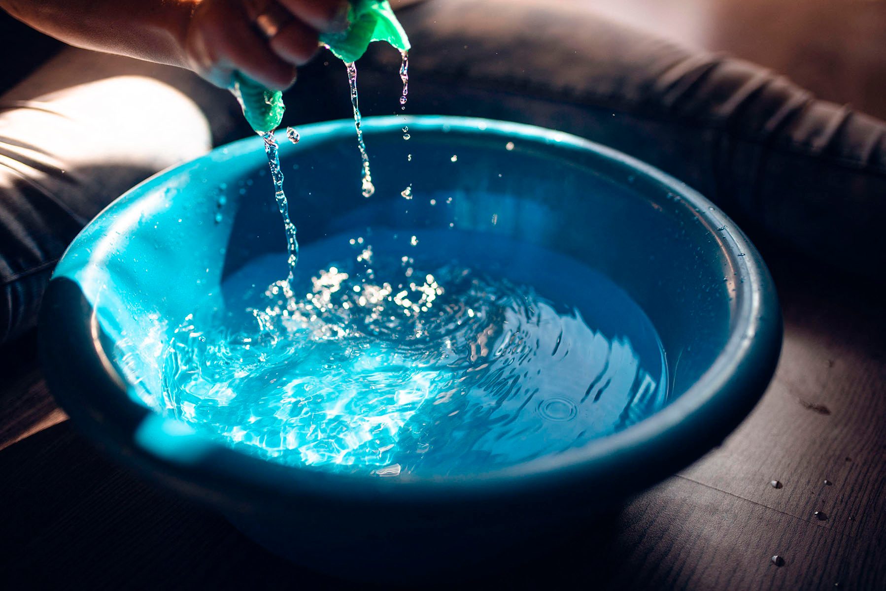 The woman squeezes a cloth over the blue bucket