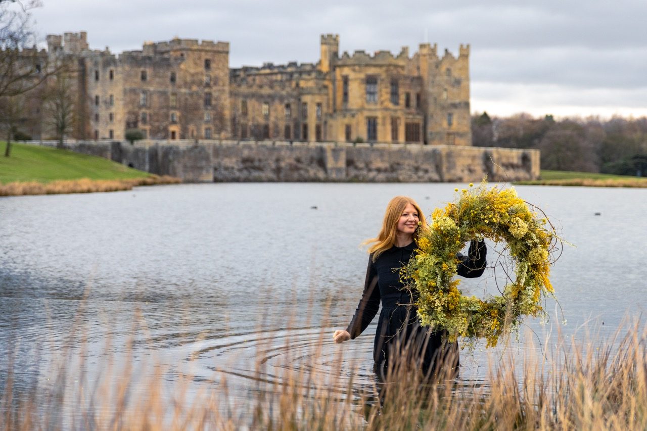Woman holding a floral wreath in front of Raby Castle, Park and Gardens