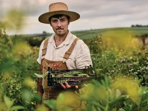Flowers growing in field in Joshua Sparkes' garden Man holding a box of vegetables in a field