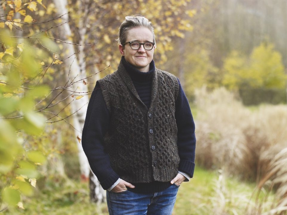 Garden designer Charlotte Harris stands in a garden with hands in pockets.