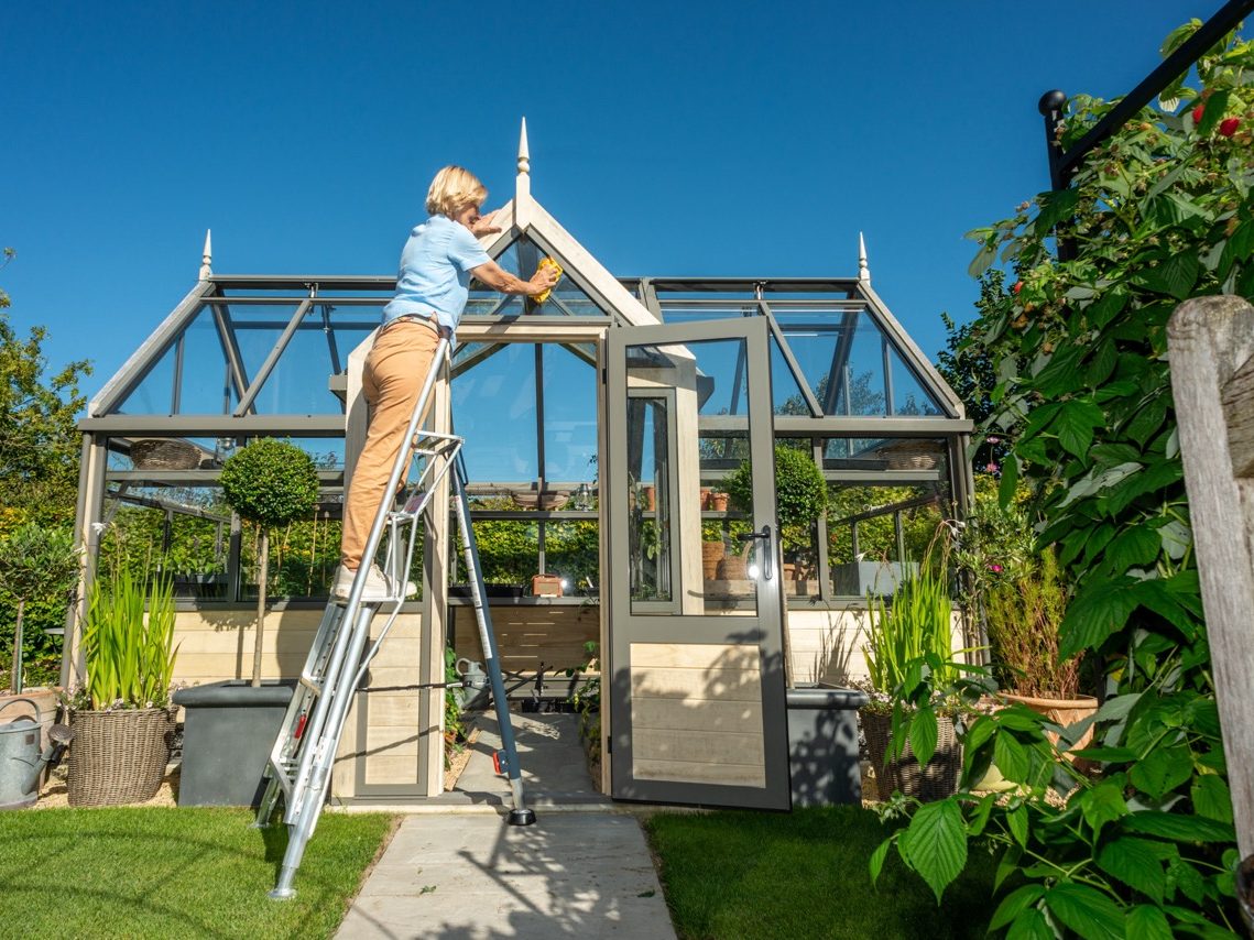 Woman stood on ladder cleaning greenhouse